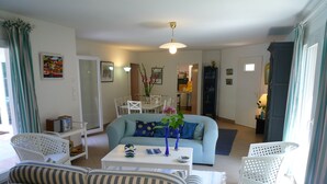 Ein Wohnzimmer mit einem gestreiften Sofa, einem hellblauen Sofa und einem Couchtisch mit Dekoration. Im Hintergrund stehen weiße Stühle und ein Esstisch.