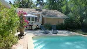 Ein Schwimmbecken mit Fliesen umrandet, ein Patio-Tisch mit Stühlen und ein Blumentopf.