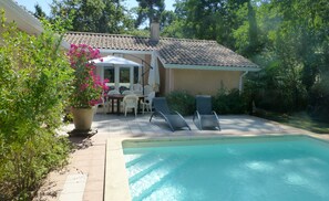 A swimming pool with a tiled deck, a patio table with chairs, and a potted plant.