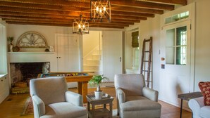 Una sala de estar acogedora con una mesa de billar, dos sillones, una chimenea y techo de madera.