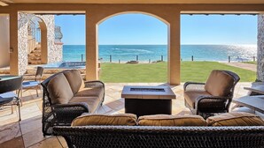 A covered outdoor seating area with wicker furniture, a fire pit, and a view of the ocean.