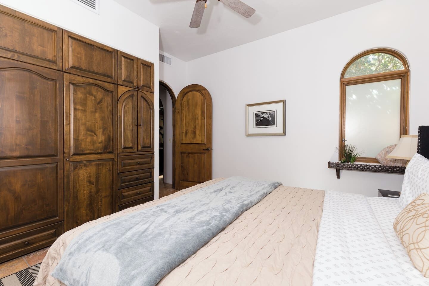 Une chambre avec une grande armoire en bois, un lit avec une literie à motifs, une petite table de chevet et un miroir au-dessus du lit.