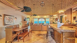 A spacious living area with a large window overlooking the sea, a wooden ceiling, and a bar area with a view.