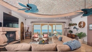 A spacious living room with a fireplace, comfortable seating, and a view of the sea.