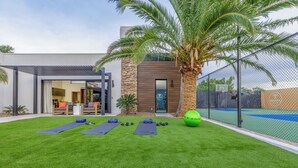A modern house with a tennis court, a palm tree, and exercise equipment on the lawn. - Experience luxury in Central Scottsdale with heated pool, pickleball, & slide! (Scottsdale)