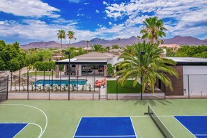A tennis court with a pool, palm trees, and mountains in the background. - Experience luxury in Scottsdale with heated pool, hot tub, pickleball, & slide! (Scottsdale)