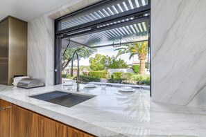 A modern kitchen with a built-in sink, a stainless steel range hood, and a window overlooking a landscaped garden. - Experience luxury in Scottsdale with heated pool, hot tub, pickleball, & slide! (Scottsdale)