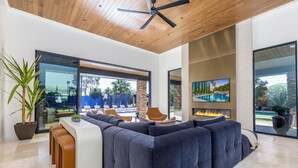 A modern living room with a large sectional sofa, a wooden ceiling, and a large window overlooking a pool. - Experience luxury in Central Scottsdale with heated pool, pickleball, & slide! (Scottsdale)