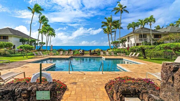 A pool area with lounge chairs, palm trees, and a view of the ocean. - Poipu Kapili 12 By Parrish Kauai - oceanfront, end unit, sunset views, close to (Koloa)
