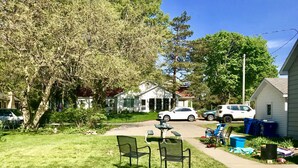 A residential area with a lawn, two chairs, a picnic table, and a white house in the background.