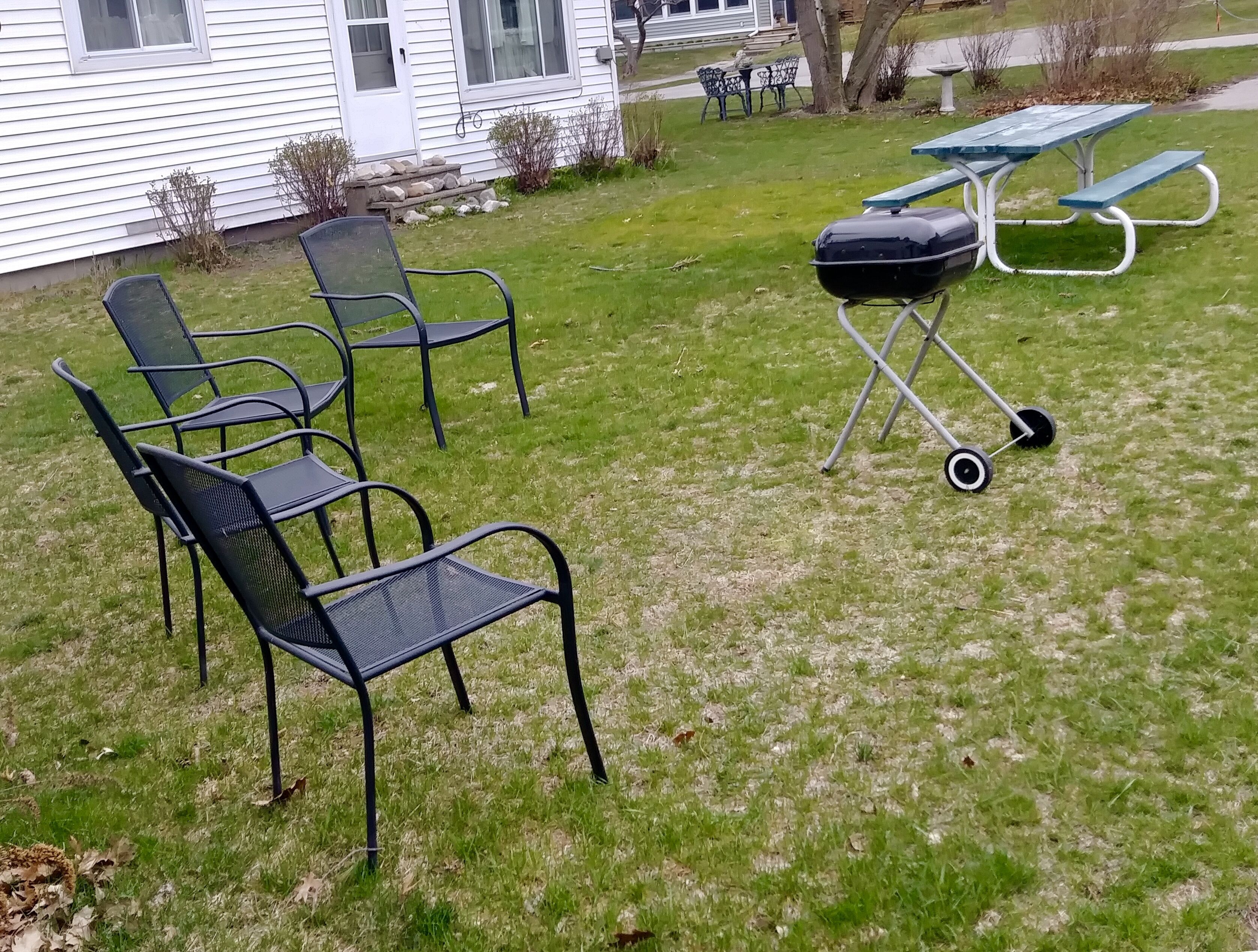 Une cour arrière verdoyante avec un barbecue, une table de pique-nique et des chaises d’extérieur.
