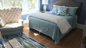 Un dormitorio con cama, una silla, una lámpara y vistas a árboles a través de la ventana.