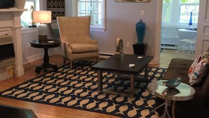 Una sala de estar con chimenea, un sillón color crema, una mesa de centro y un tapete estampado.