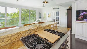 A modern kitchen with a marble countertop, gas stove, and pendant lighting.