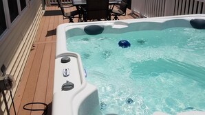 A hot tub on a wooden deck with a white fence and outdoor furniture.