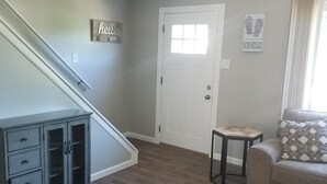 A living room with a grey sofa, a small table, a cabinet, a staircase, and a door with a window.