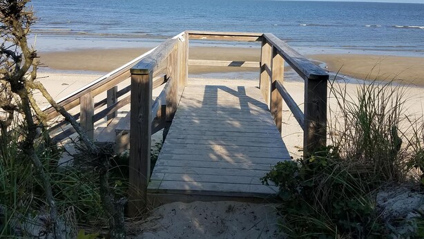 A wooden boardwalk leading to a beach with clear skies.