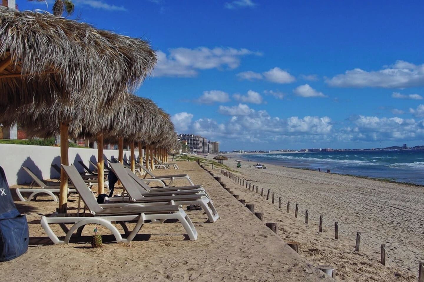 Une plage avec des transats et des parasols en chaume, une plage de sable fin et un ciel bleu dégagé.