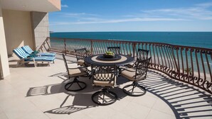 Un balcon avec une table ronde et des chaises, une petite table ronde sur laquelle se trouve un saladier rempli de fruits, et deux fauteuils de relaxation.