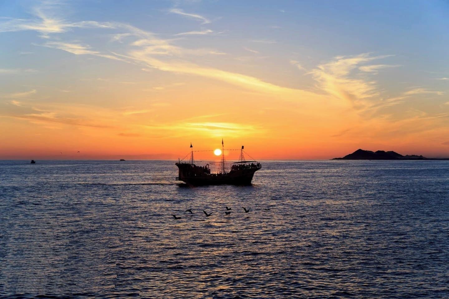 A sunset over the ocean with a ship in the foreground and a distant island.