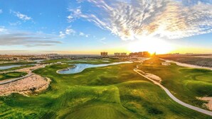 Vue aérienne d’un terrain de golf avec une rivière, des sentiers et des bâtiments situés au loin.