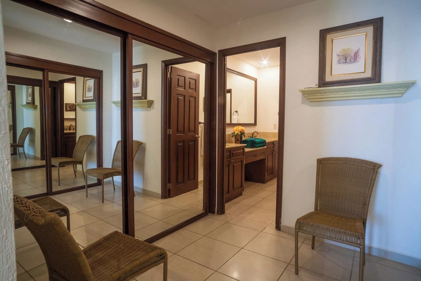 Una habitación con un espejo grande, un florero verde y una silla de mimbre.