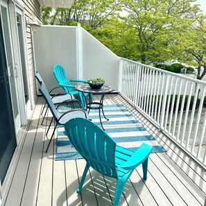 A wooden deck with turquoise chairs and a small table, surrounded by a white railing.