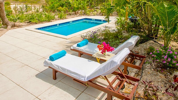 Un espace piscine comprenant deux chaises longues et une petite table sur laquelle est posé un vase de fleurs.