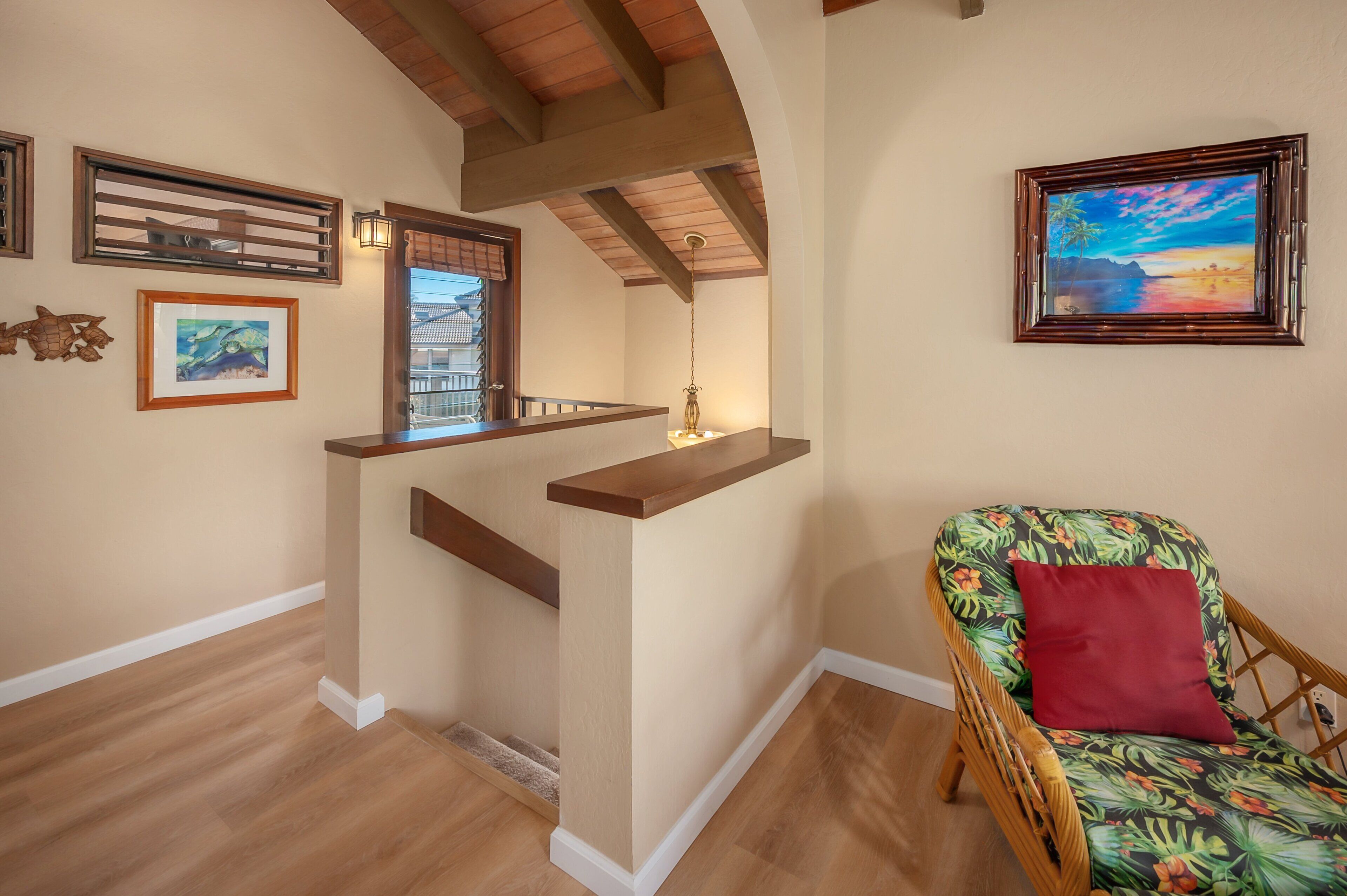 A wooden staircase with a railing, a wicker chair with a red cushion, and framed artwork on the walls.