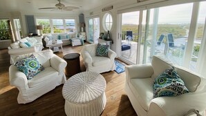 A spacious living area with white furniture, large windows, and a view of the beach. -  Beautiful, Gulf-Front Home on Bean Point--Halcyon House (Anna Maria)