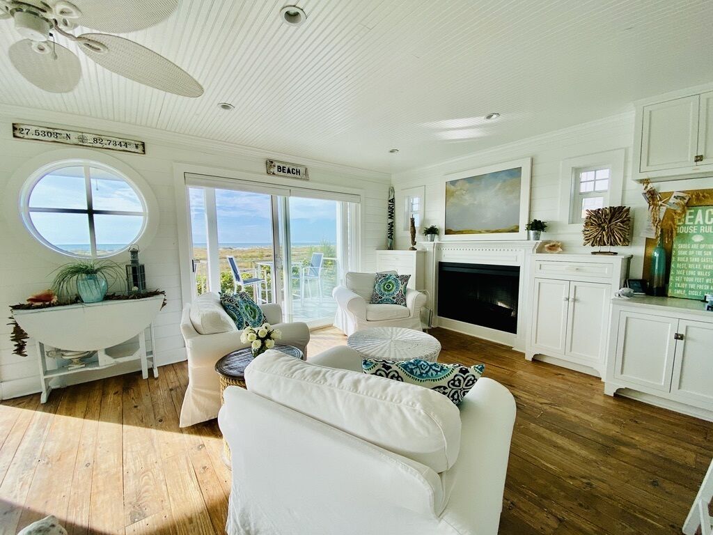 A spacious living room with a fireplace, white furniture, and a view of the beach.