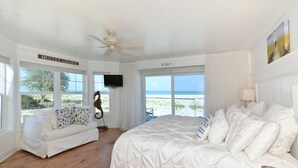 A bedroom with a large bed, a white sofa, a ceiling fan, and a TV. -  Beautiful, Gulf-Front Home on Bean Point--Halcyon House (Anna Maria)