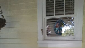 A porch with two white chairs with red cushions, a small round table with a potted plant, and a window with blinds. - The Rohde Guest House (St Augustine)