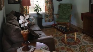 A living room with a brown leather sofa, a green patterned armchair, a small wooden coffee table, and a ceiling fan. - The Rohde Guest House (St Augustine)