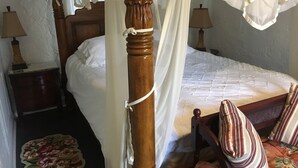 A bedroom with a four-poster bed, a bedside table, a lamp, and a floral rug. - The Rohde Guest House (St Augustine)