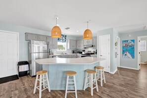 Una cocina moderna con una isla central, armarios blancos, electrodomésticos de acero inoxidable y taburetes de madera.