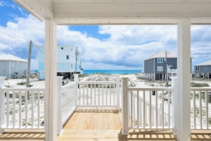 A wooden deck with white railings, a view of the beach, and buildings in the background.