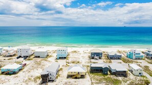 A beachfront property with multiple buildings, some with elevated structures, and a clear view of the ocean. - Gulf Views | Beach Access | Classic Coastal Cottage (Gulf Shores)