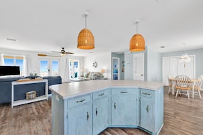 A modern kitchen with a large island, pendant lights, and a dining area with a wooden table and chairs.