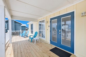 A covered porch with wooden flooring, blue doors, and white railings.
