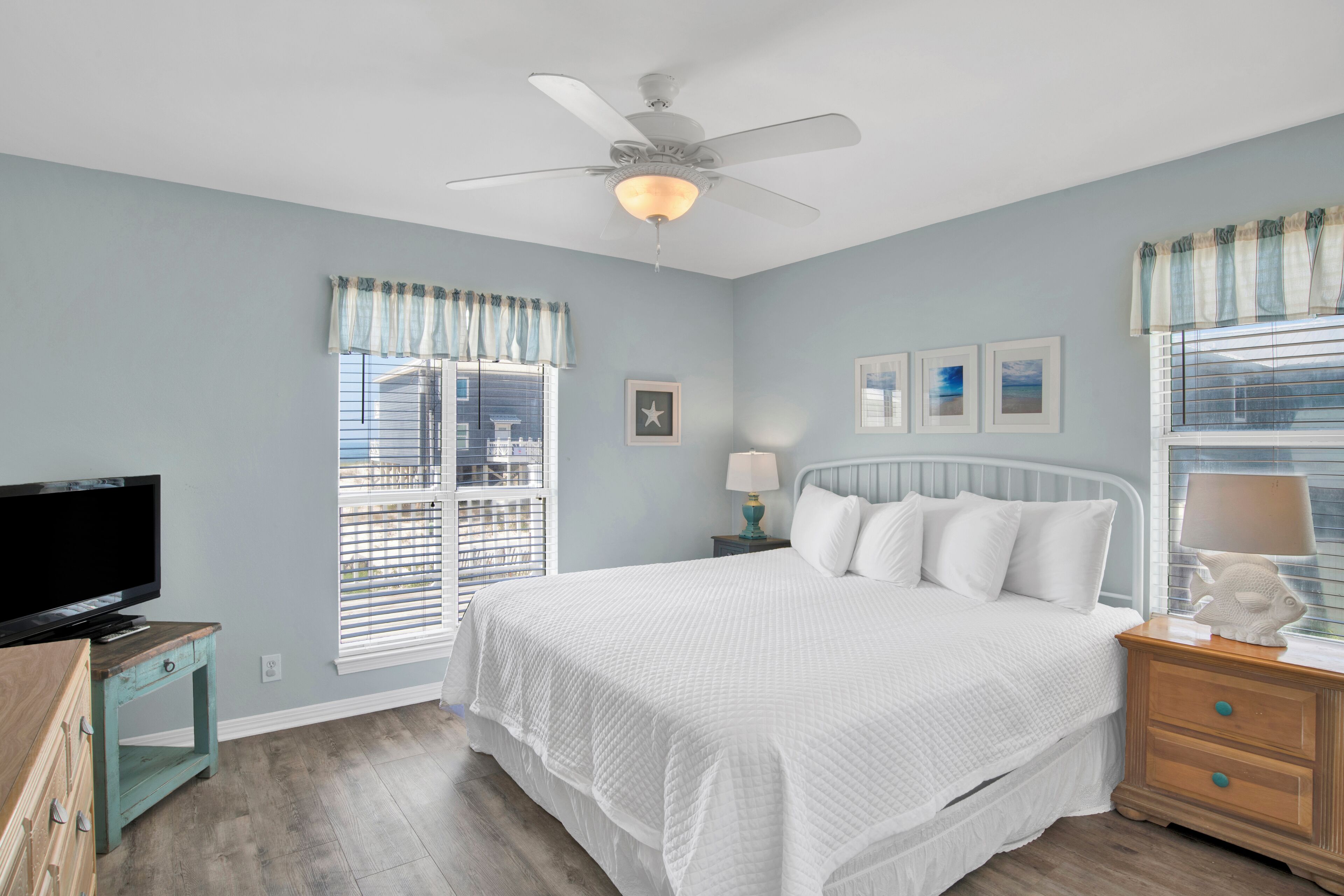 A bedroom with a bed, a ceiling fan, a TV, and a window with blinds.