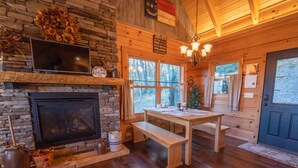 A cabin interior with a stone fireplace, wooden dining table, benches, and a cozy atmosphere. - Family-Friendly Log Cabin with Hot Tub, Fire Pit & Game Room – Pet Welcome! (Hendersonville)