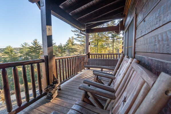 A wooden deck with benches, a railing, and a view of trees.