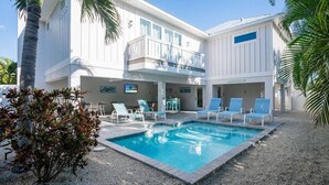 Ein zweistöckiges Gebäude mit Pool, Liegestühlen und einer Palme.