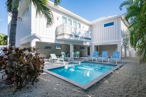 Ein zweistöckiges Gebäude mit Pool, Liegestühlen und einer Palme.