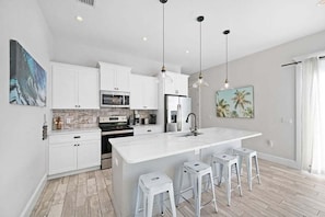 Une cuisine moderne avec des meubles blancs, un grand îlot central, des tabourets de bar et des luminaires suspendus.