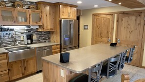 A modern kitchen with wooden cabinets, stainless steel appliances, and a central island with bar stools. - short walk to Quicksilver lift, bars & restaurants. (Breckenridge)