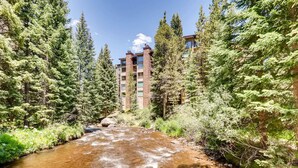 A river flowing through a forest with a multi-story building in the background. - short walk to Quicksilver lift, bars & restaurants. (Breckenridge)