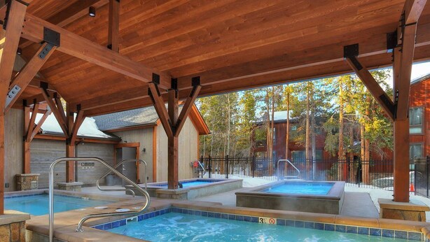A covered outdoor swimming pool with multiple hot tubs, wooden beams, and a view of a forested area. - short walk to Quicksilver lift, bars & restaurants. (Breckenridge)
