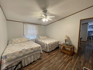 Un dormitorio con dos camas, un ventilador de techo, una mesita de noche con lámpara y una ventana con persianas.